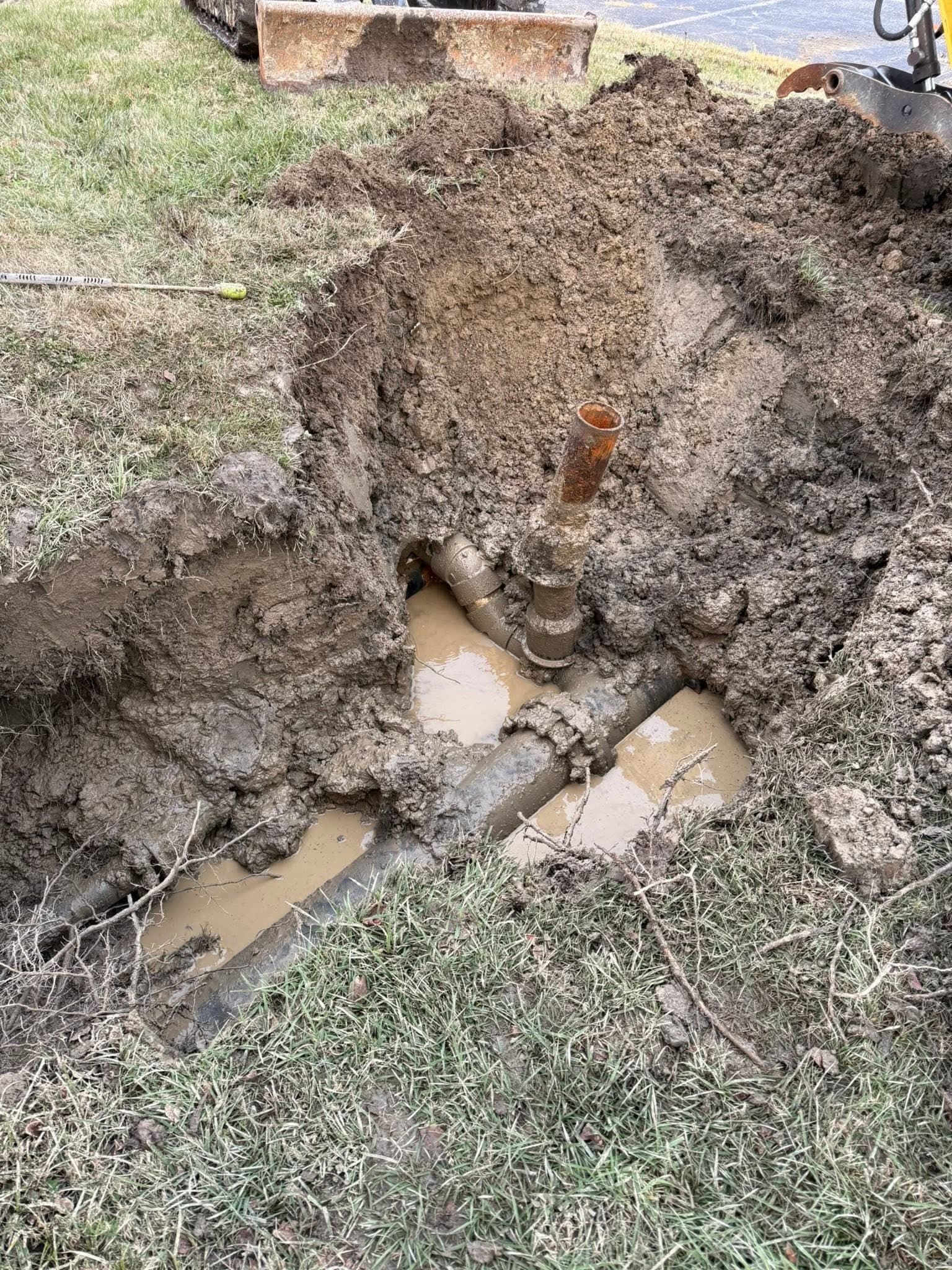 Excavated trench exposing a rusted underground pipe connection and standing water at a Portsmouth VA property — Newman's Plumbing Service & Repair
