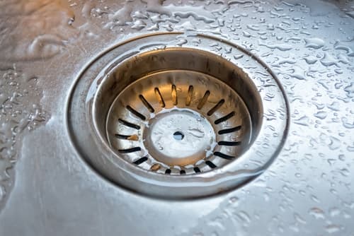 Plumber clearing a blocked kitchen drain line inside a Portsmouth VA home — Newman's Plumbing Service & Repair
